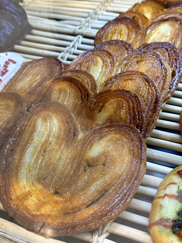 Stock photo showing close-up, elevated view of bakery shelf display with rows of freshly baked heart shaped, palmier pastries available for purchasing.