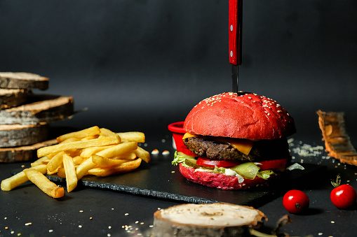 A hamburger with a knife sticking out of it is placed next to a serving of french fries.
