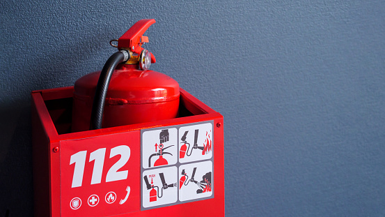 A bright red fire extinguisher is stored inside a red box marked with the emergency number 112 and usage instructions.