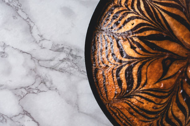 Zebra cake with a chocolate stripes pattern placed on a white marble tabletop in a cake pan, high-angle view photo with copy space.