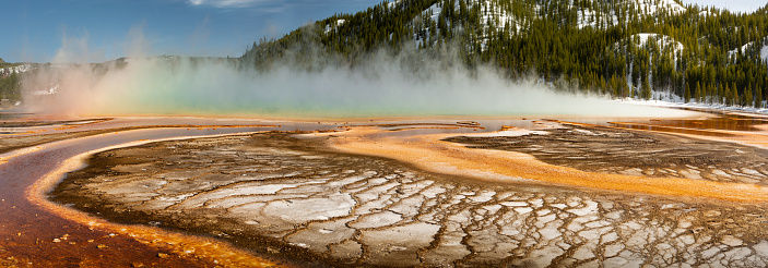 Grand prismatic spring Overlook in Yellowstone shows vibrant colors of a hot spring with mineral deposits and a steam rainbow in the background