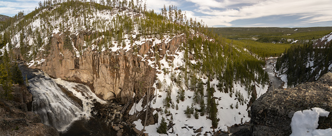 An enchanting image of a powerful waterfall cascading through a snow-covered landscape, cutting through the rugged cliffs surrounded by pine trees