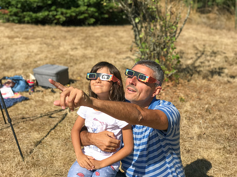 Father and daughter looking at the sun during a solar eclipse on a country park, family outdoor activity.