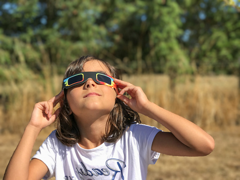A young girl looking at the sun during a solar eclipse on a country park, family outdoor activity.