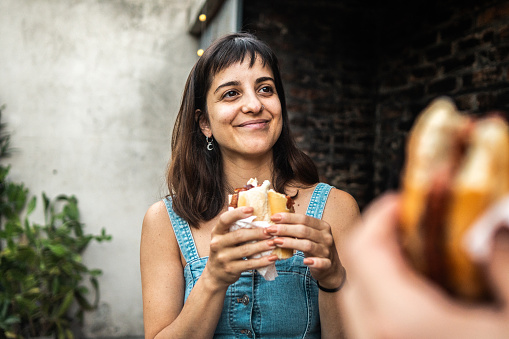 Mid adult woman talking and eating choripán with friend in the backyard at home