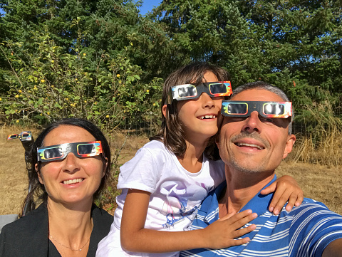 Father, mother and daughter, family viewing solar eclipse with special glasses in a park.