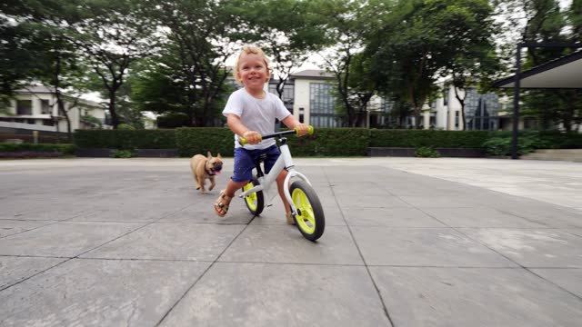 Joyful toddler starts and races on runbike in suburban square, slow motion shot