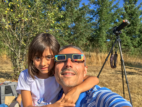 Father and daughter looking at the sun during a solar eclipse on a country park, family outdoor activity.