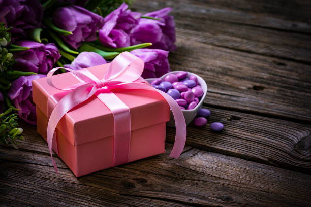 素朴な木製のテーブルの上にピンク色のギフトボックス、キャンディー、花。母の日のコンセプト