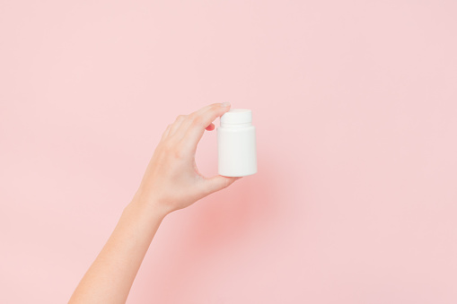 View on white bottle plastic tube in hands on a pink background. Packaging for pills, capsules, supplements or ointment. Cosmetics