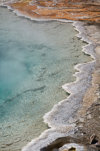 Vibrant hot spring with steaming water, surrounded by colorful mineral deposits in Fountain Paint Pot Trail in Yellowstone National Park