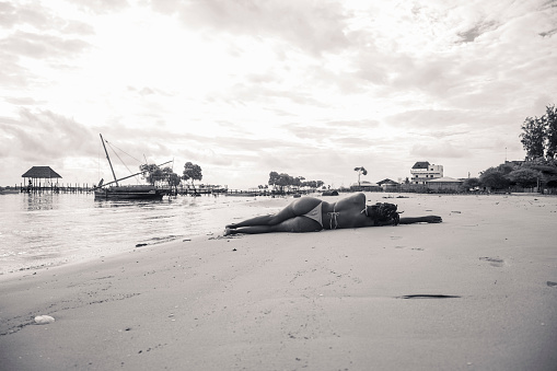 A young black woman in a bikini sunbathing on the sand along the beach