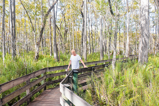 Woman with blonde hair walks on a boardwalk through the Six Mile Cypress Slough Preserve in southwest Florida, USA.