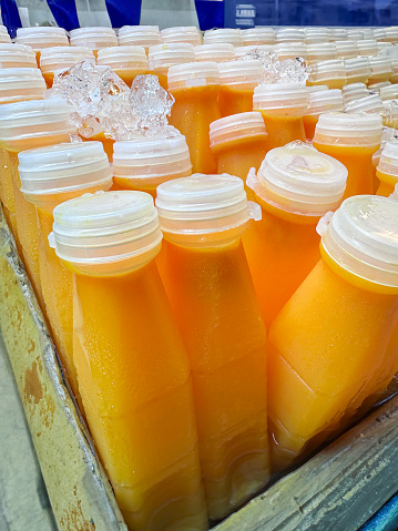 Stock photo showing close-up view of box filled with ice cubes and containing plastic bottles of orange fruit juices being kept chilled.