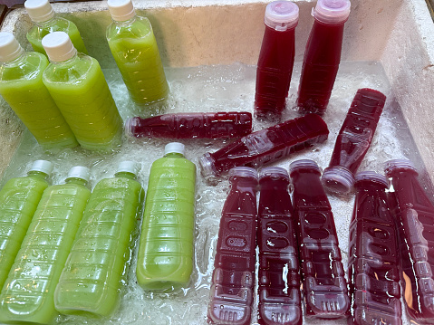 Stock photo showing close-up, elevated view of polystyrene box filled with ice cubes and containing plastic bottles of avocado and beetroot smoothies being kept chilled.