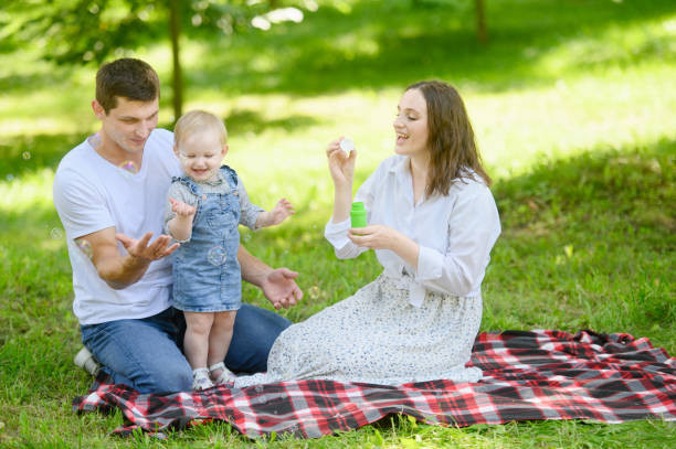 istock Happy family blowing soap bubbles while sitting on a blanket during a picnic in the park. Smiling parents and child spend leisure time together. Summer time concept, outdoor recreation. 2058486149