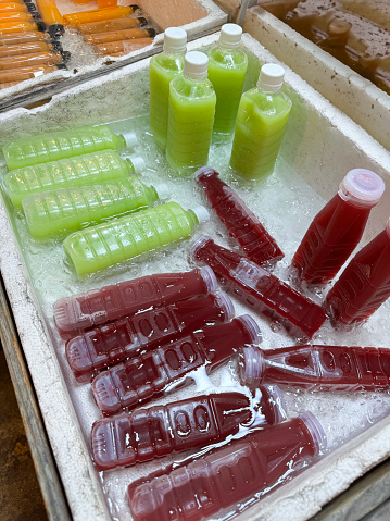 Stock photo showing close-up, elevated view of polystyrene boxes filled with ice cubes and containing plastic bottles of orange juice, carrot, avocado and beetroot smoothies being kept chilled.