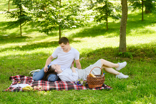 Romantic man and woman relax in nature during a date, look at each other, the woman lies on the man leg. Concept of love and tender relationships. Valentine's Day.
