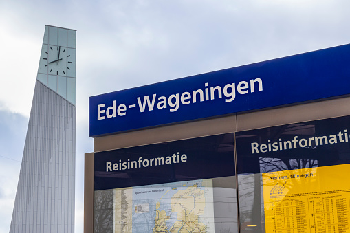 Ede, The Netherlands - March 1, 2024: Information panel with clock tower in the background at new Ede-Wageningen Central Station which was developed based on sustainability principles.