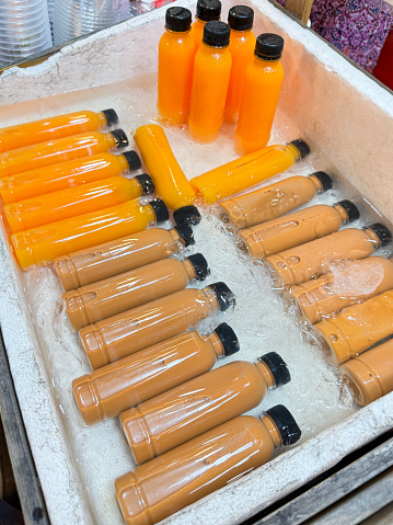 Stock photo showing close-up, elevated view of polystyrene boxes filled with ice cubes and containing plastic bottles of orange and carrot juices being kept chilled.