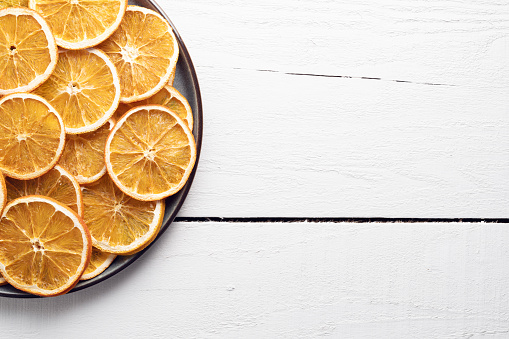 Dry orange slices in plate on wooden background