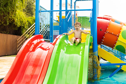Child on colorful water slide at playground. Summer fun and water games concept. Design for banner, poster, invitation