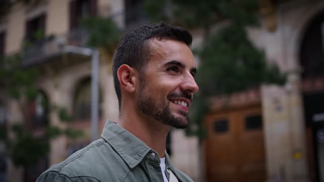 Close up side view millennial bearded attractive man walking smiling in European Barcelona city.