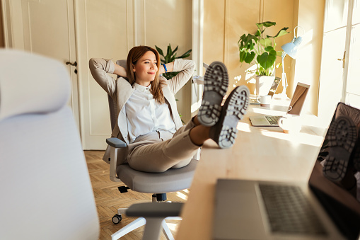 Happy young businesswoman relaxing sitting at desk with laptop in office