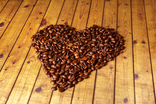 Heart shape made from coffee beans on wooden surface.