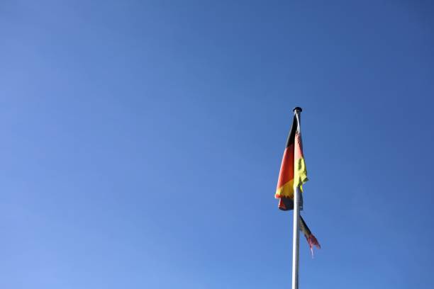 broken torn disastrous German flag on a flagpole in front of a blue sky with open space
