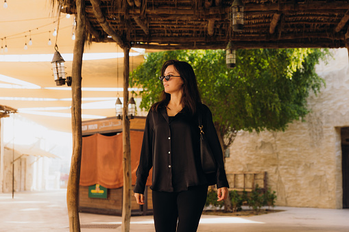Front view of female in black casual clothes walking the old streets with authentic Persian buildings at Al Bastakya district of Dubai city, United Arab Emirates