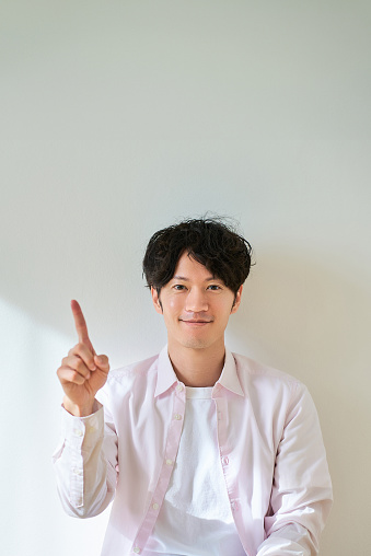 A young man posing with his index finger raised in front of a white background