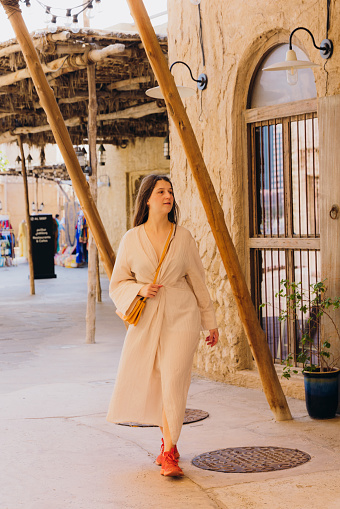 Beautiful female in traditional Arabic dress walking the old streets with authentic Persian buildings at Al Bastakya district of Dubai city, United Arab Emirates
