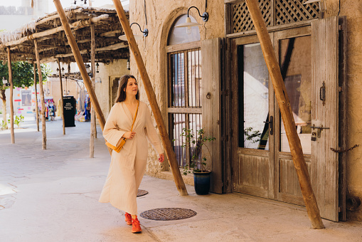 Beautiful female in traditional Arabic dress walking the old streets with authentic Persian buildings at Al Bastakya district of Dubai city, United Arab Emirates