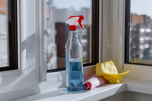 Accessories for cleaning windows. Сleanser sprayer and pink and yellow rag, microfiber cloth on the windowsill and outside the window city street