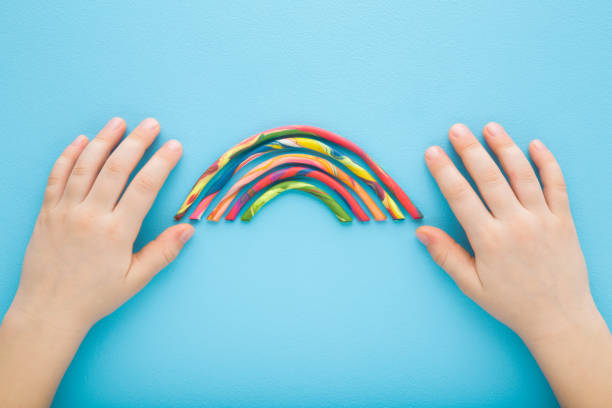 istock Baby boy hands and colorful rainbow from modeling clay on light blue table background. Pastel color. Closeup. Point of view shot. Toddler development. Top down view. 2058691788