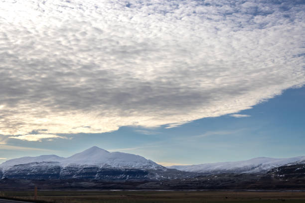 Nature with pastures and meadows. Mountains covered by snow in the highest parts. Blue sky with big white cloud. Area of Siduvegur, North-West Iceland.