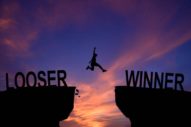 silhouette young man jumping and raising up her hand about winner concept on winner text over a beautiful sunset or sunrise at the sea. background for success winner and looser concept. - winner looser stock-fotos und bilder