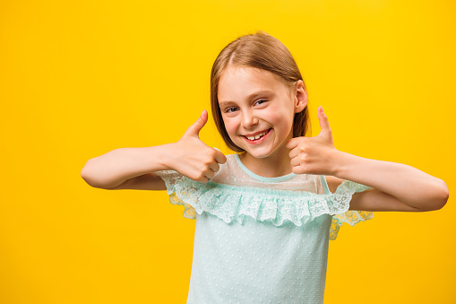 Like and approval. Studio portrait of stylish little children girl gesturing thumbs up and looking at camera. smiling to camera, yellow background