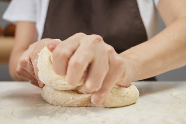 istock Unknown woman wearing brown apron kneading dough on table sprinkled with flour preparing for baking bread 2058759220