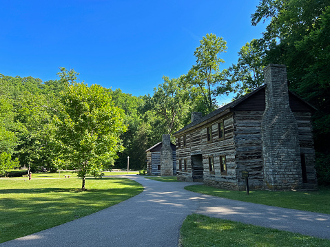 Mitchell, Indiana, USA - June 20, 2022:  Weaver’s Shop and Granny White House in the recreated, restored 1800 Pioneer Village at Spring Mill State Park, Mitchell, Indiana with beautiful blue sky copy space and vivid green trees and grass.