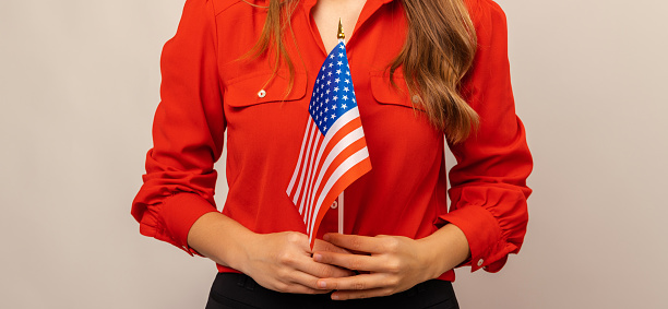 Faceless shot of a young woman wearing red shirt holding USA flag with both hands.