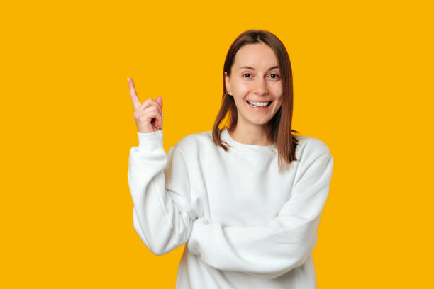 istock Smiling young woman with her arms crossed points upward at copy space. 2058836722