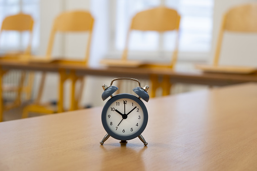 A small alarm clock on a desk in an empty classroom, symbolizing school time or learning timetable
