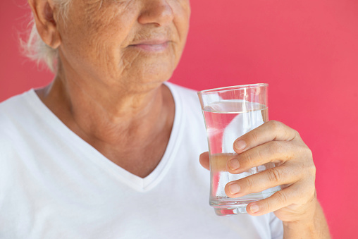 Senior woman drinking water in front of pink background.