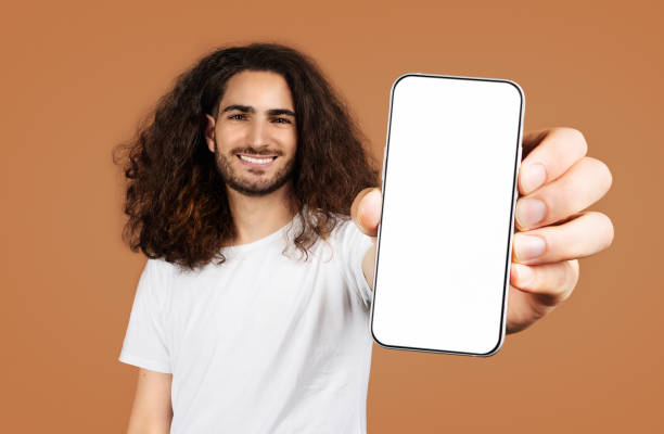 istock man with curly hair showing large smartphone screen, beige backdrop 2058952803