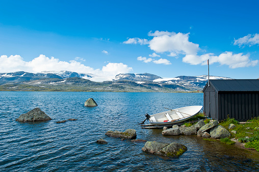 Beautiful landscape with a boat on the shore of Lake Finsevatnet, snowy mountains and glacier Hardangerjokulen in Finse in Norway