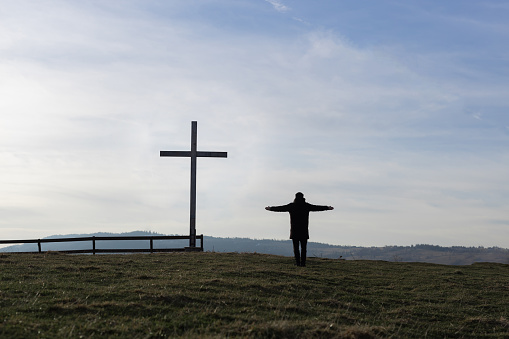 Religion theme, view of catholic cross and man silhouette, with fantastic view and mountains as background