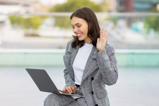 istock lady engaged in video call on laptop waving hand outside 2058960301