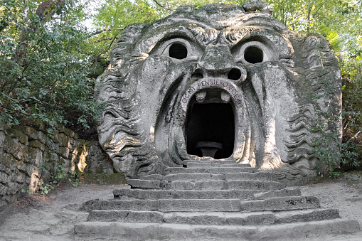 Bomarzo, Italy - 10 08 2023: Head figure with open mouth entrance sculptured in giant rocks in Bomarzo Sacro Bosco Park in Italy
